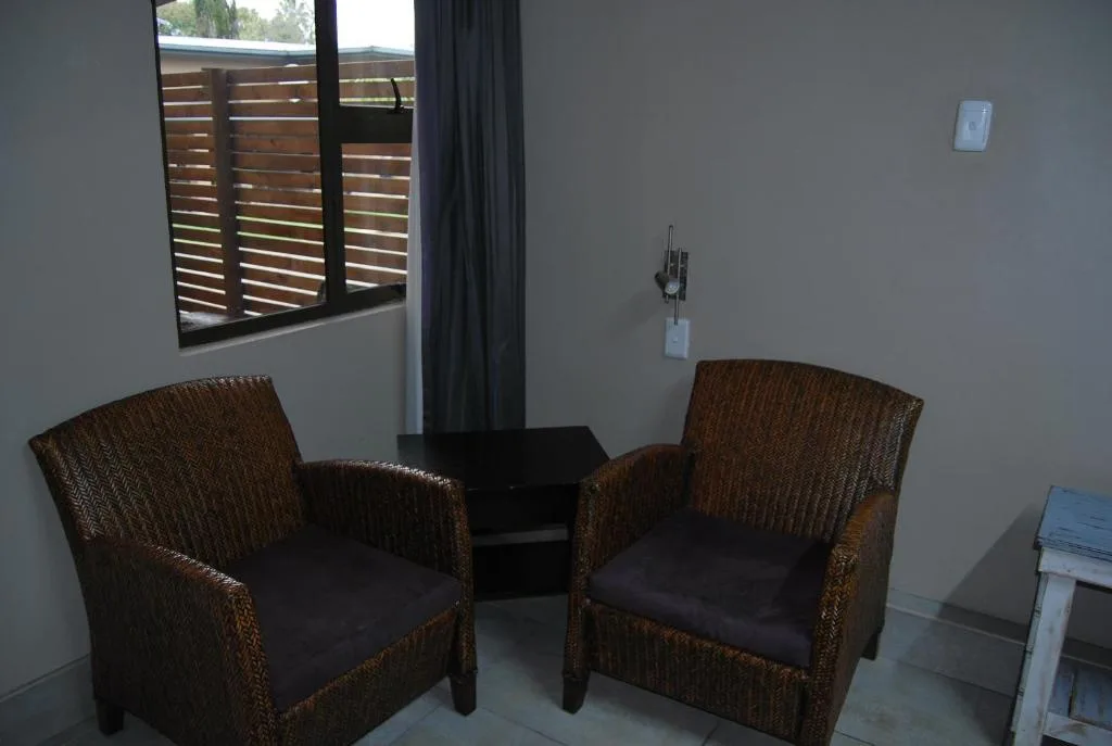 Two woven armchairs with black cushions facing small table near window