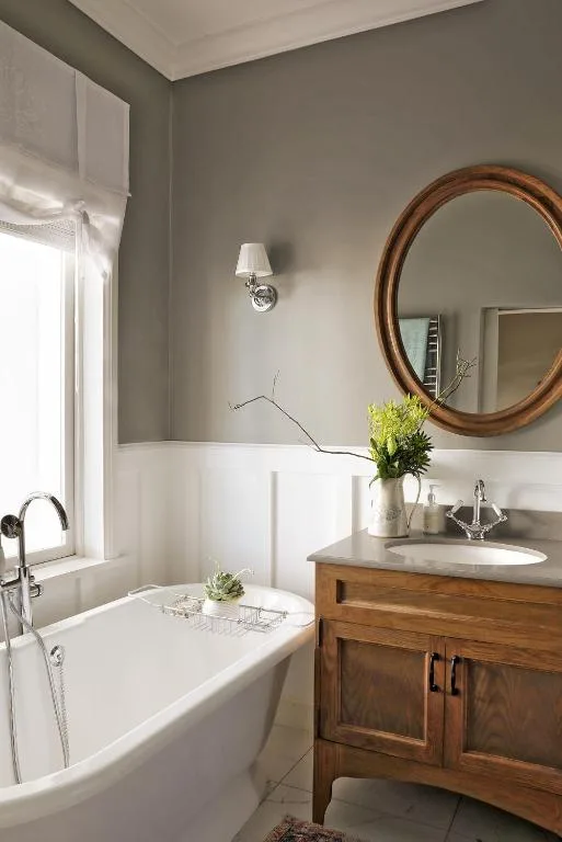 Bright bathroom with freestanding tub, wooden vanity, and round mirror