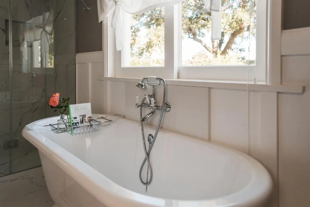 Freestanding white bathtub with vintage fixtures near bright windows