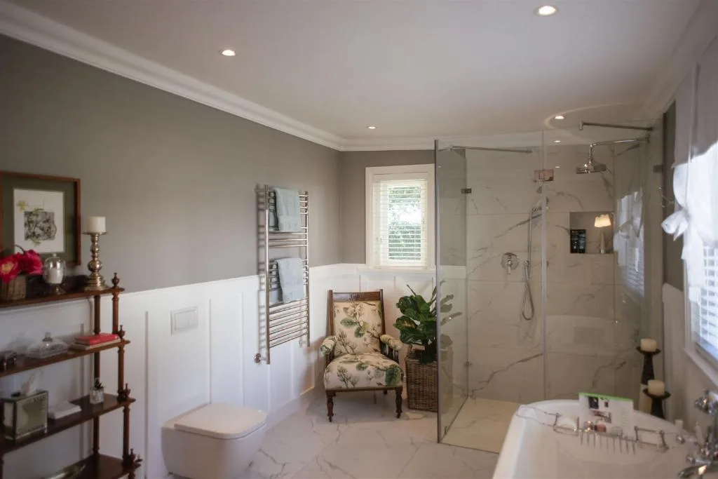 Spacious ensuite bathroom with marble floors, glass shower enclosure, and elegant seating