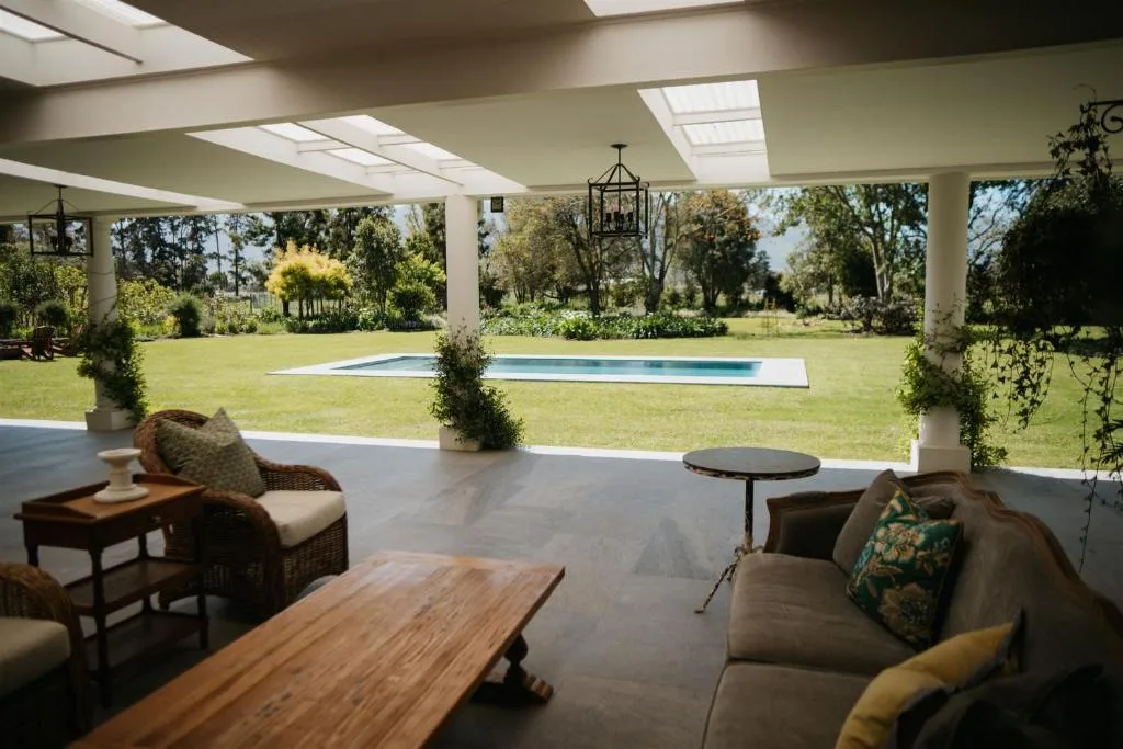 Covered patio with seating overlooking pool and manicured gardens