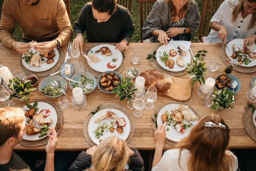 Group of guests enjoying a meal together at a wooden dining table outdoors