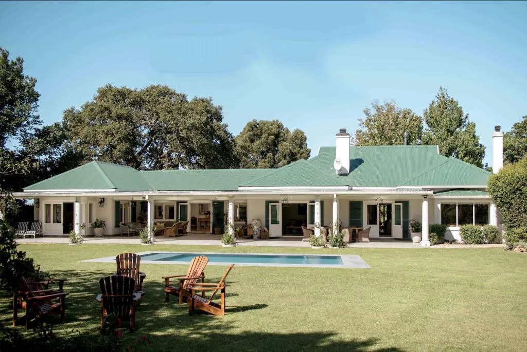 White colonial-style villa with green roof and manicured lawn, pool in foreground