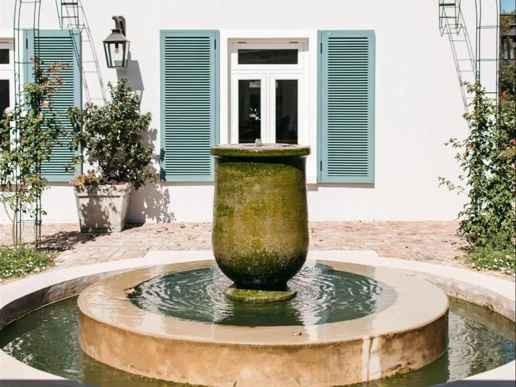 White building facade with turquoise shutters and decorative water fountain courtyard