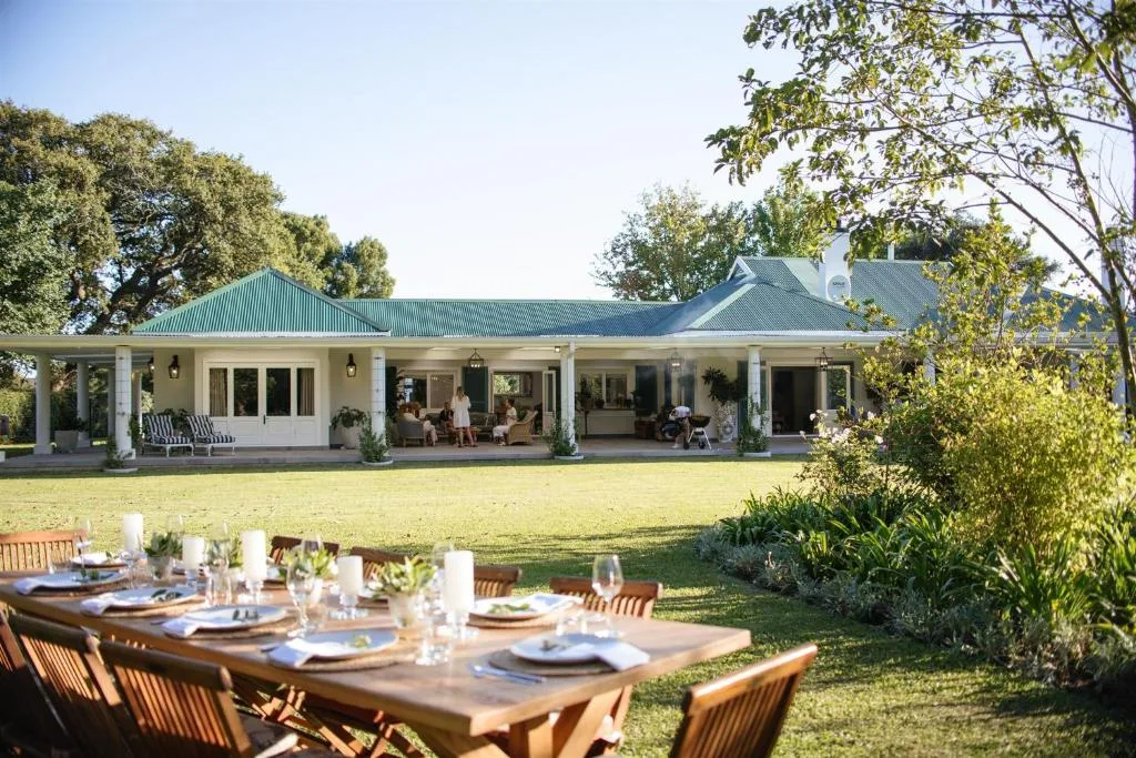 Modern white farmhouse with green roof and spacious veranda overlooking manicured lawn