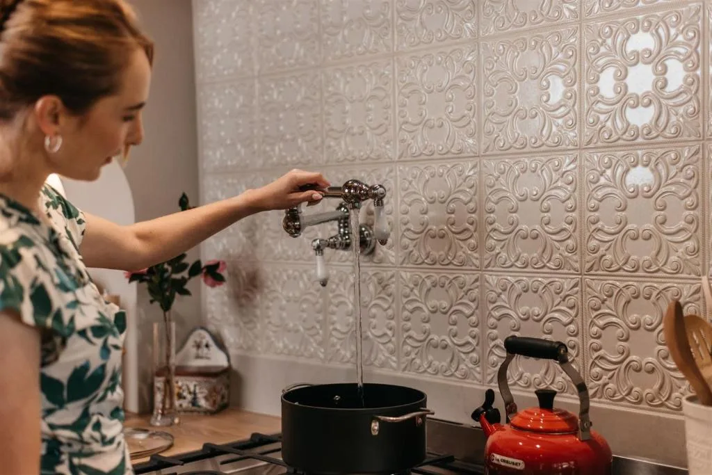 Woman filling pot with water at kitchen sink with decorative tile backsplash