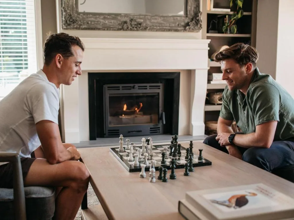 Two men playing chess in lounge with fireplace and built-in shelving
