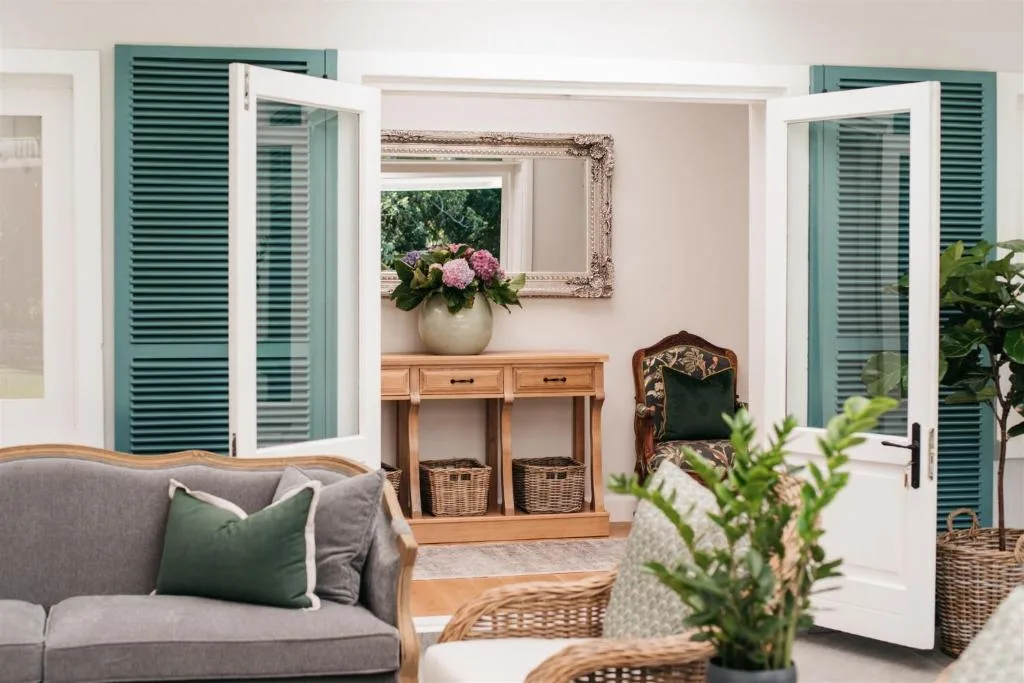 Light-filled lounge with gray sofa, wooden console table, and garden views through French doors
