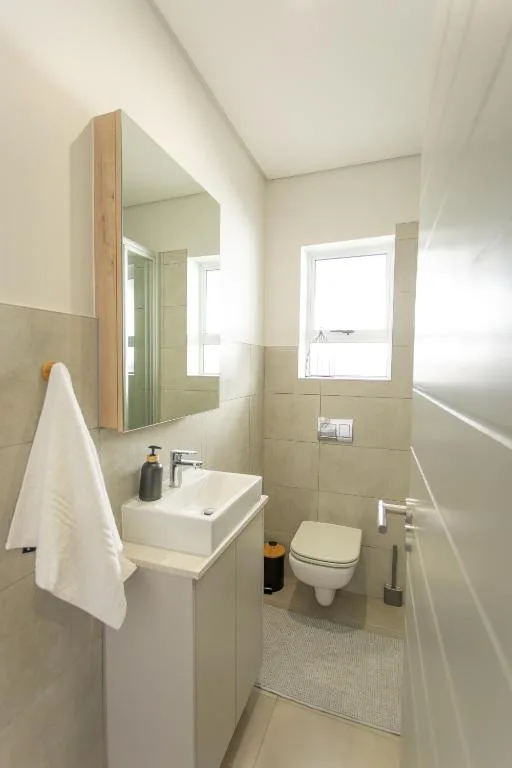 Modern bathroom with white sink, toilet, mirror cabinet and bright window