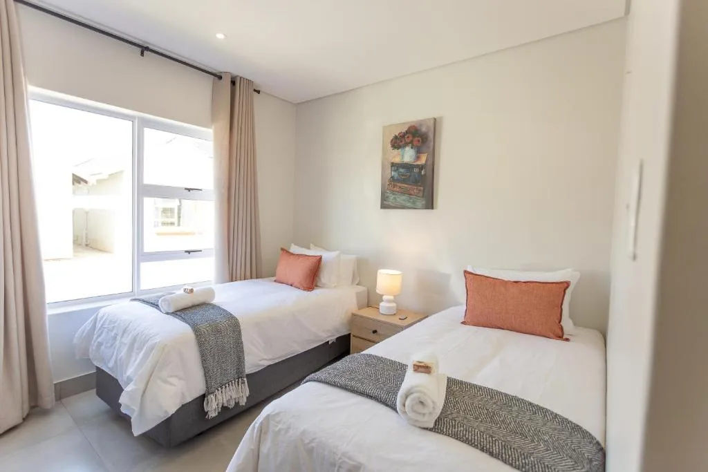 Twin bedroom with white bedding, orange accent pillows, and bright window
