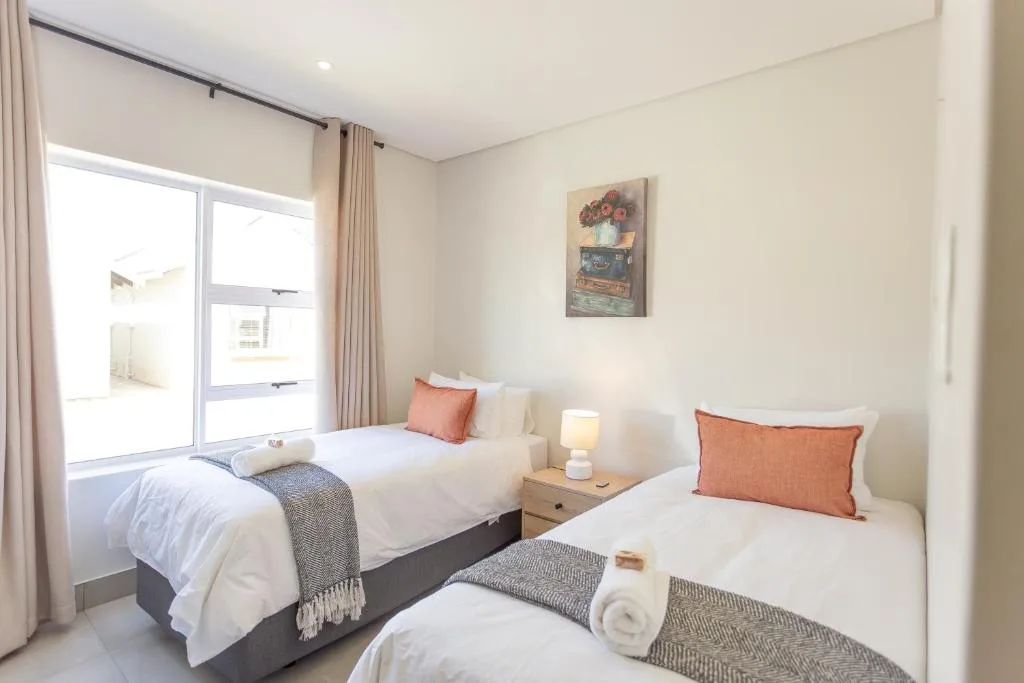 Bright twin bedroom with white bedding, orange accents, and large windows