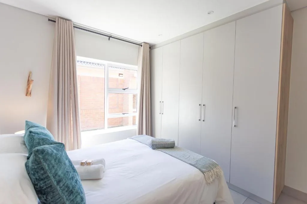 Bright bedroom with queen bed, blue pillows, and white built-in wardrobes