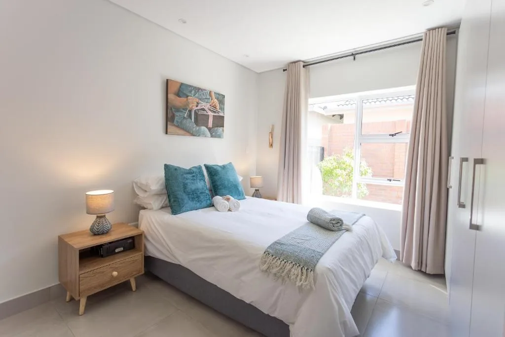 Bright bedroom with queen bed, teal pillows, wooden nightstand, and garden views
