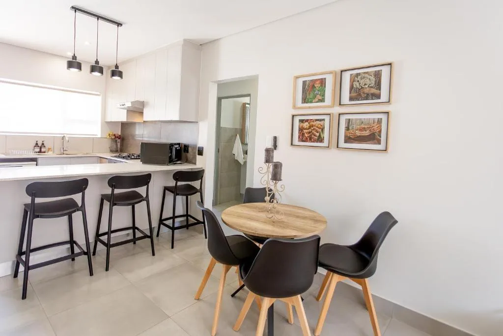 Modern dining area with wooden table, black chairs, and kitchen beyond