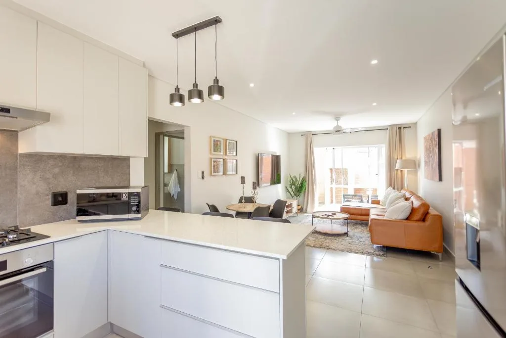Modern white kitchen with island bench and pendant lights, open to lounge