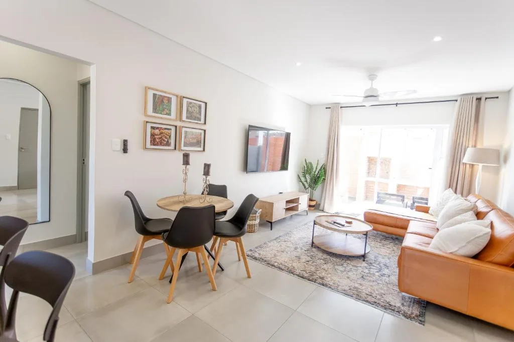 Modern lounge with tan leather sofa, dining table, TV, and large windows