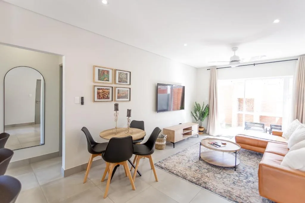 Modern lounge with dining table, sofa, TV, and bright windows overlooking deck